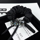 Front view of black satin hair tie with crystal-accented ribbon bow on white background